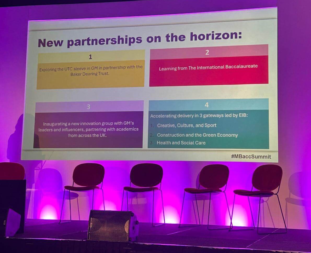 1A stage featuring several chairs arranged in front of a large screen. There is a title on the screen, 'New partnerships on the horizon' and below that four text boxes, each headed with a number 1-4. 1. Exploring the UTC sleeve in GM in partnership with the Baker Dearing Trust. 2. Learning from The International Baccalaureate 3. Inaugurating a new innovation group with GM's leaders and influencers, partnering with academics from across the UK. 4. Accelerating delivery in 3 gateways led by EIB: - Creative, Culture, and Sport - Construction and the Green Economy - Health and Social Care At the bottom-right of the screen, the words #MBaccSummit. 