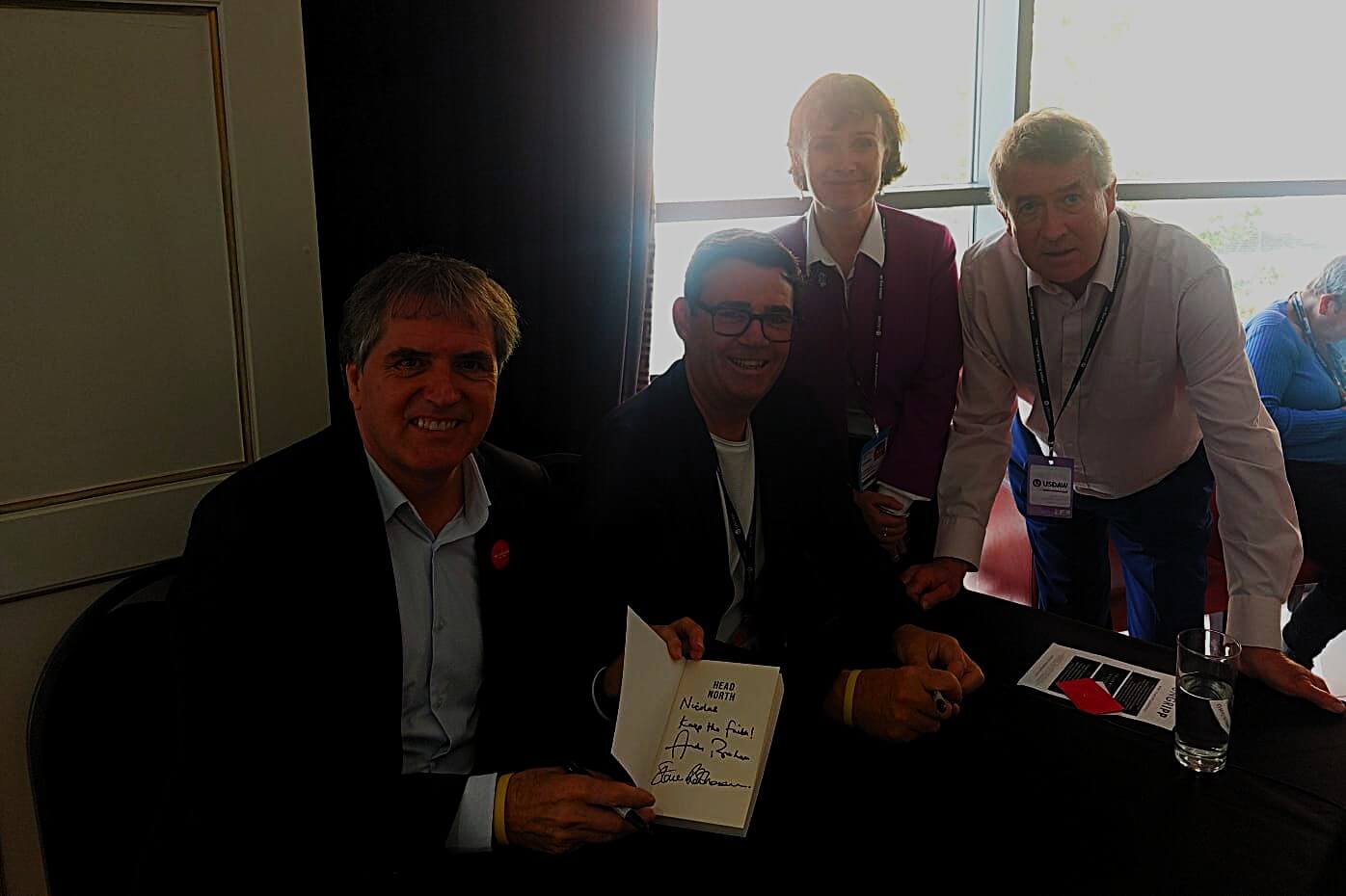 Four people - Rotheram and Burnham sitting, Kate and Nicolas standing - smiling and posing together, holding a book in front of them for a group photo.