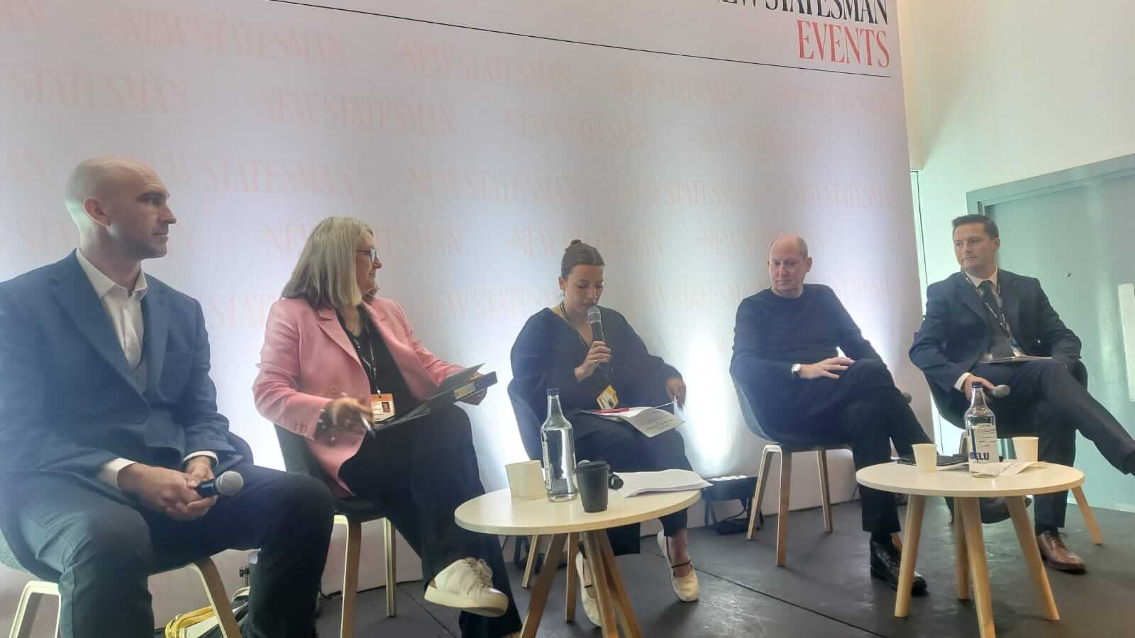 Four people seated on chairs, talking in front of a plain wall.