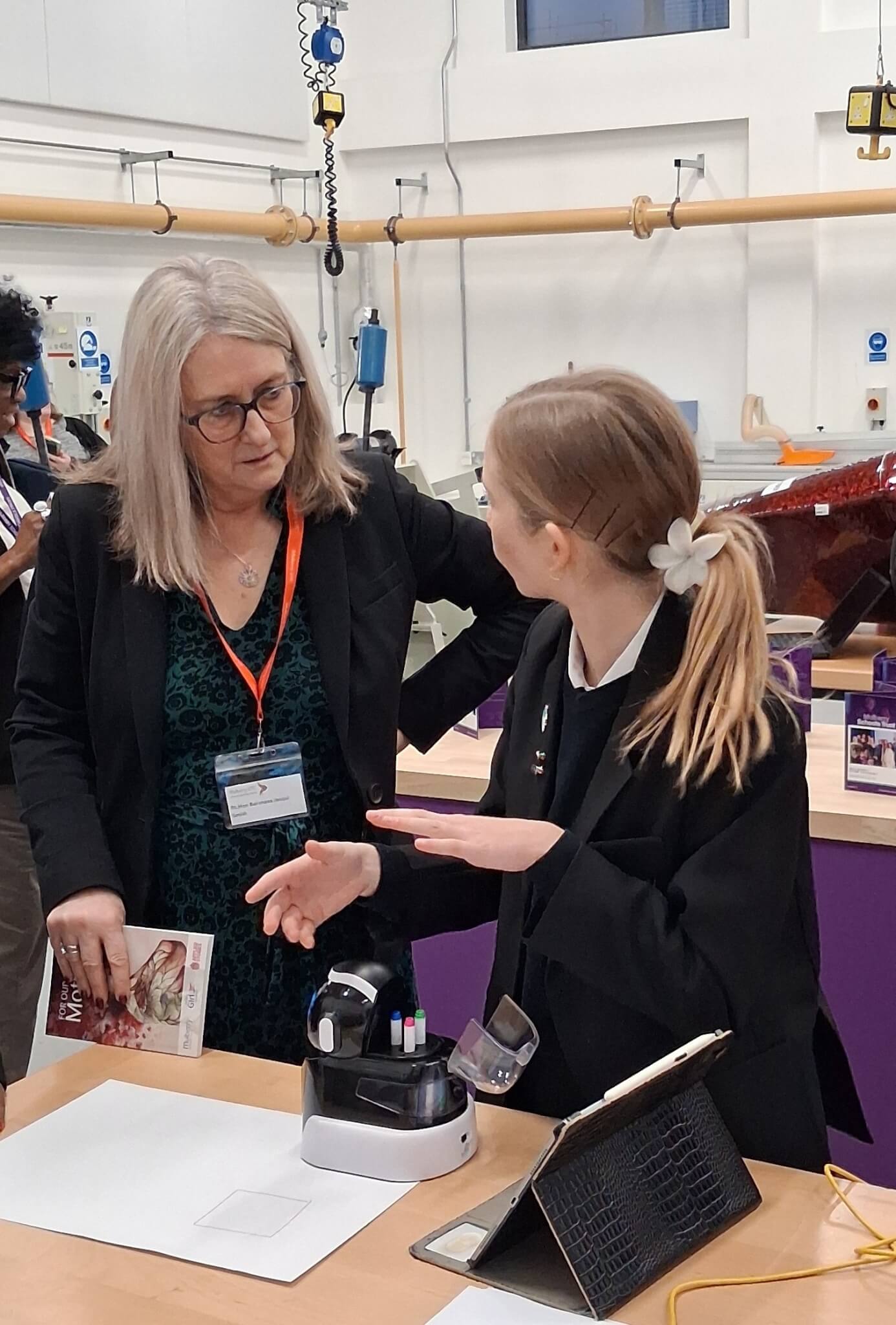A woman discussing with a young female student next to a workbench.