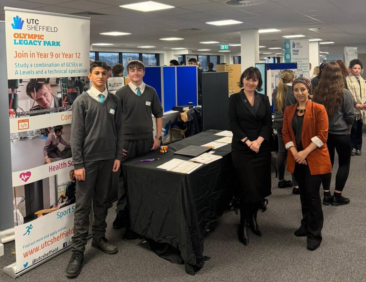 Students and adults stood before a presentation table and roller banner.