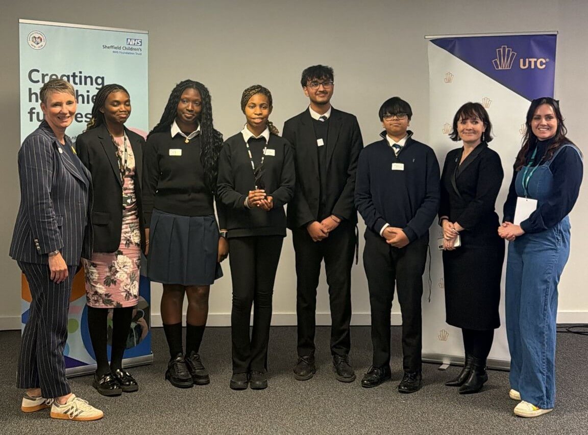 A mixed group of students stood between two roller banners for UTCs and the NHS. The students are flanked by three women.