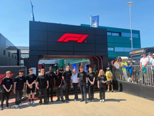 Young people stood in front of a grey gateway; the lintel adorned with a Formula 1 logo.