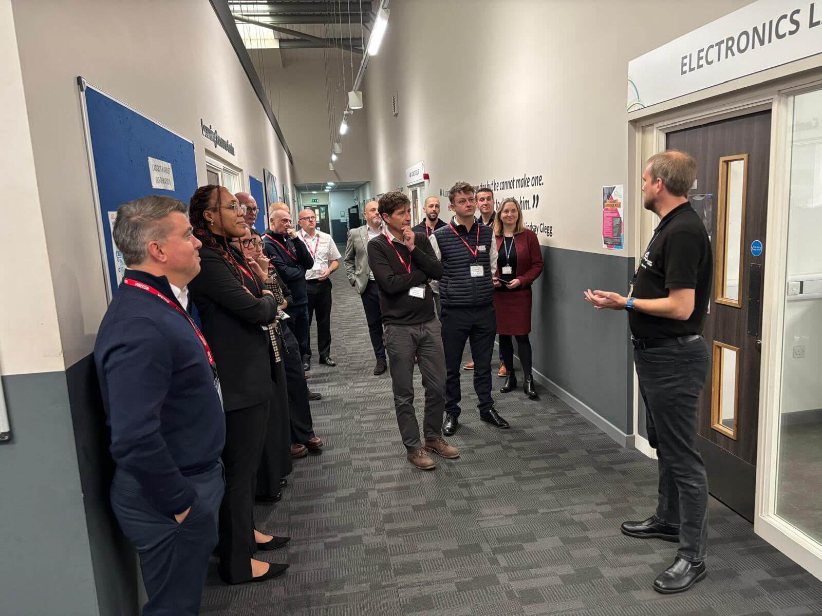 A group of people in a hallway, attentively listening to a man speaking to them.